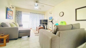 Ein Wohnzimmer mit einer Sofagarnitur, einem Fernseher, einem Ventilator und einer Wanduhr.
