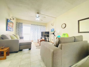 A living room with a sofa set, a television, a fan, and a clock on the wall. - Amanzimtoti Beach Accommodation (aManzimtoti)