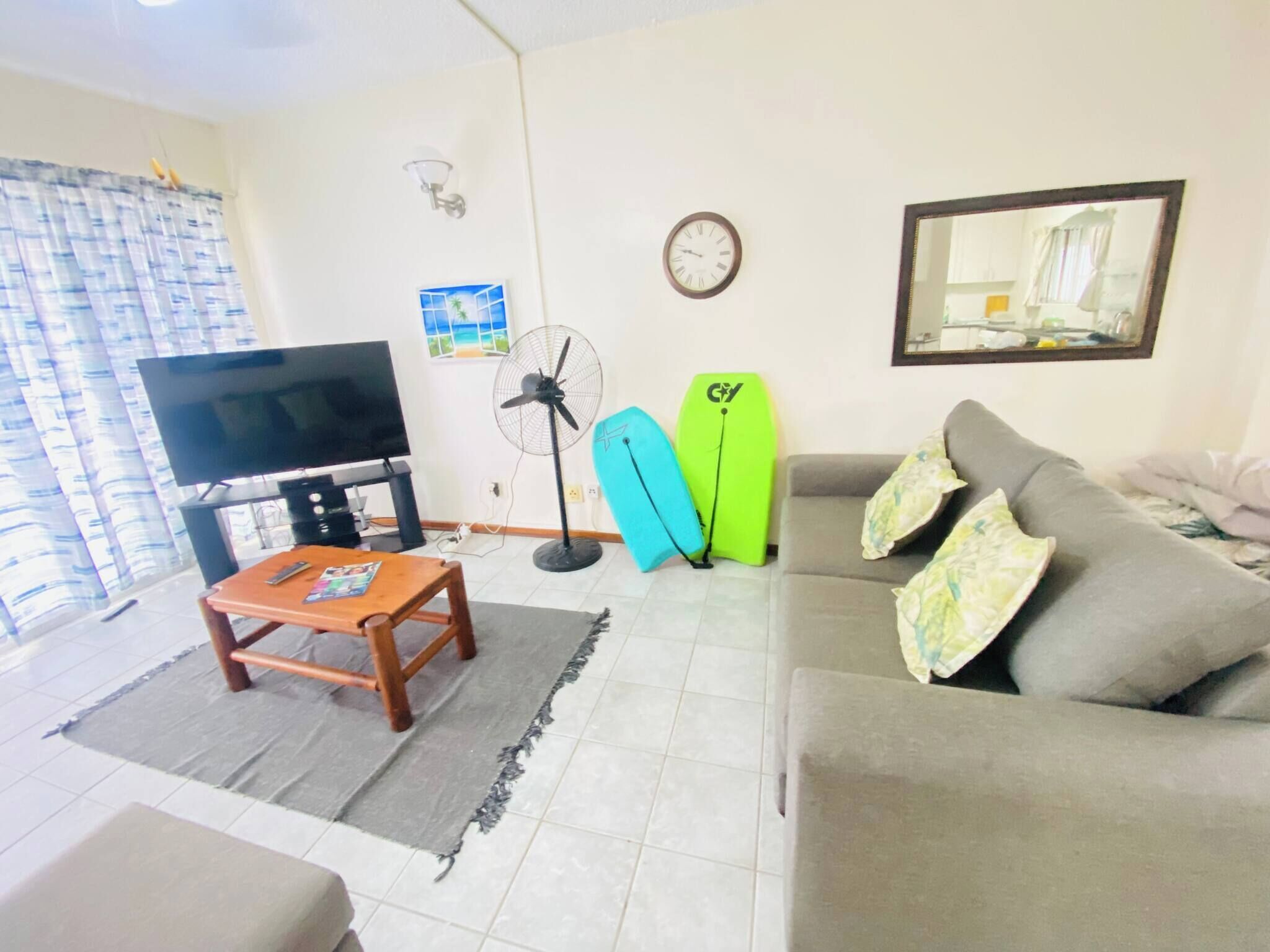 A living room with a TV, a fan, a sofa, and two surfboards.