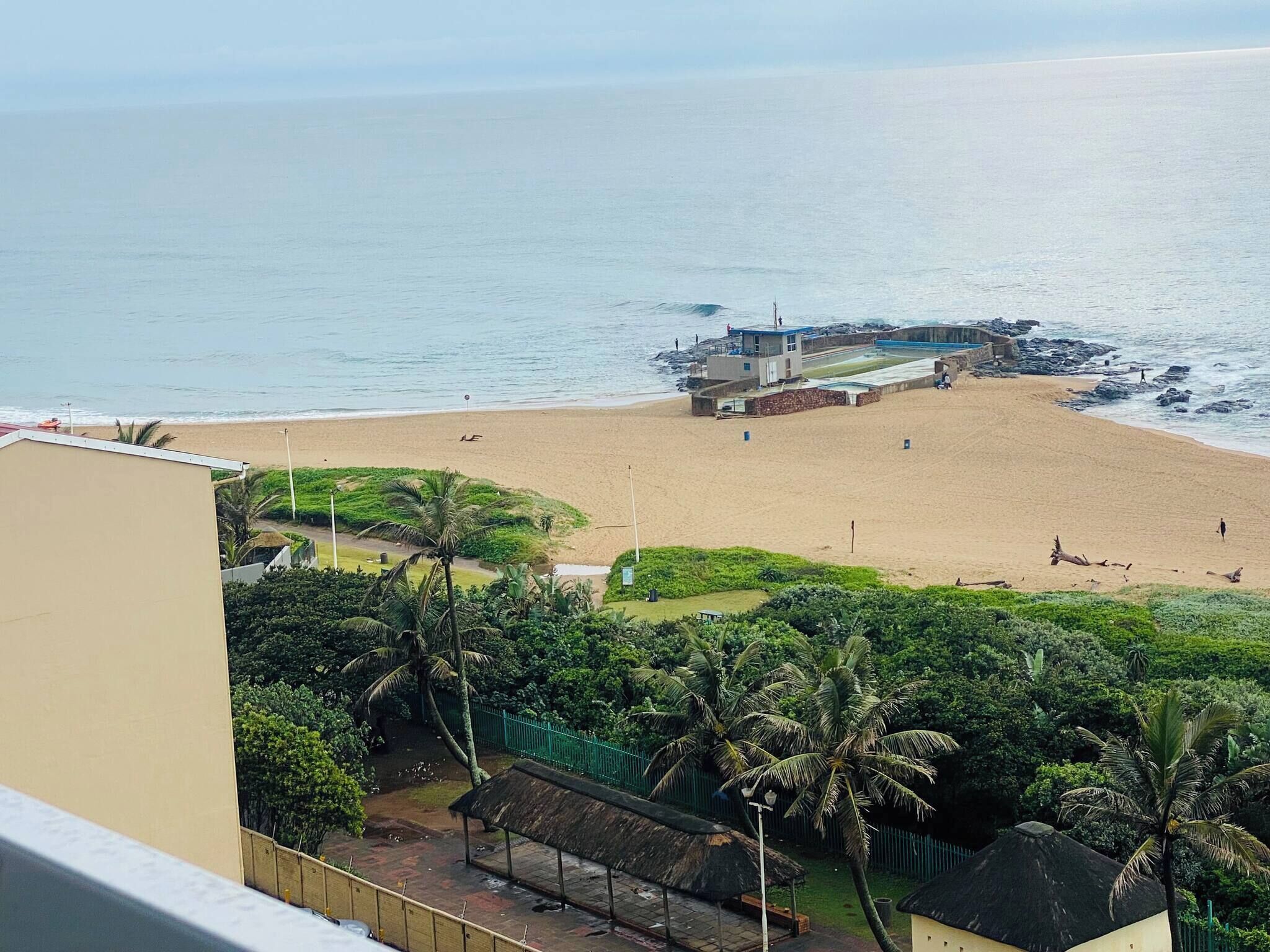 A beach with a lifeguard tower, palm trees, and a building in the foreground.