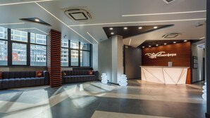 Una moderna zona de recepción con un mostrador de madera, un área de estar con sofás y grandes ventanales que ofrecen vistas al exterior.