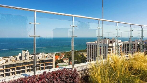 Un edificio alto con barandilla de vidrio que domina un paisaje urbano costero.