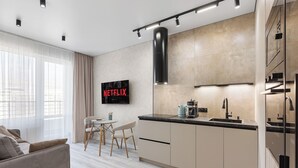 Una cocina moderna con horno empotrado, cafetera y lavamanos. Hay un comedor con mesa y sillas. Un televisor en la pared muestra el logotipo de Netflix.