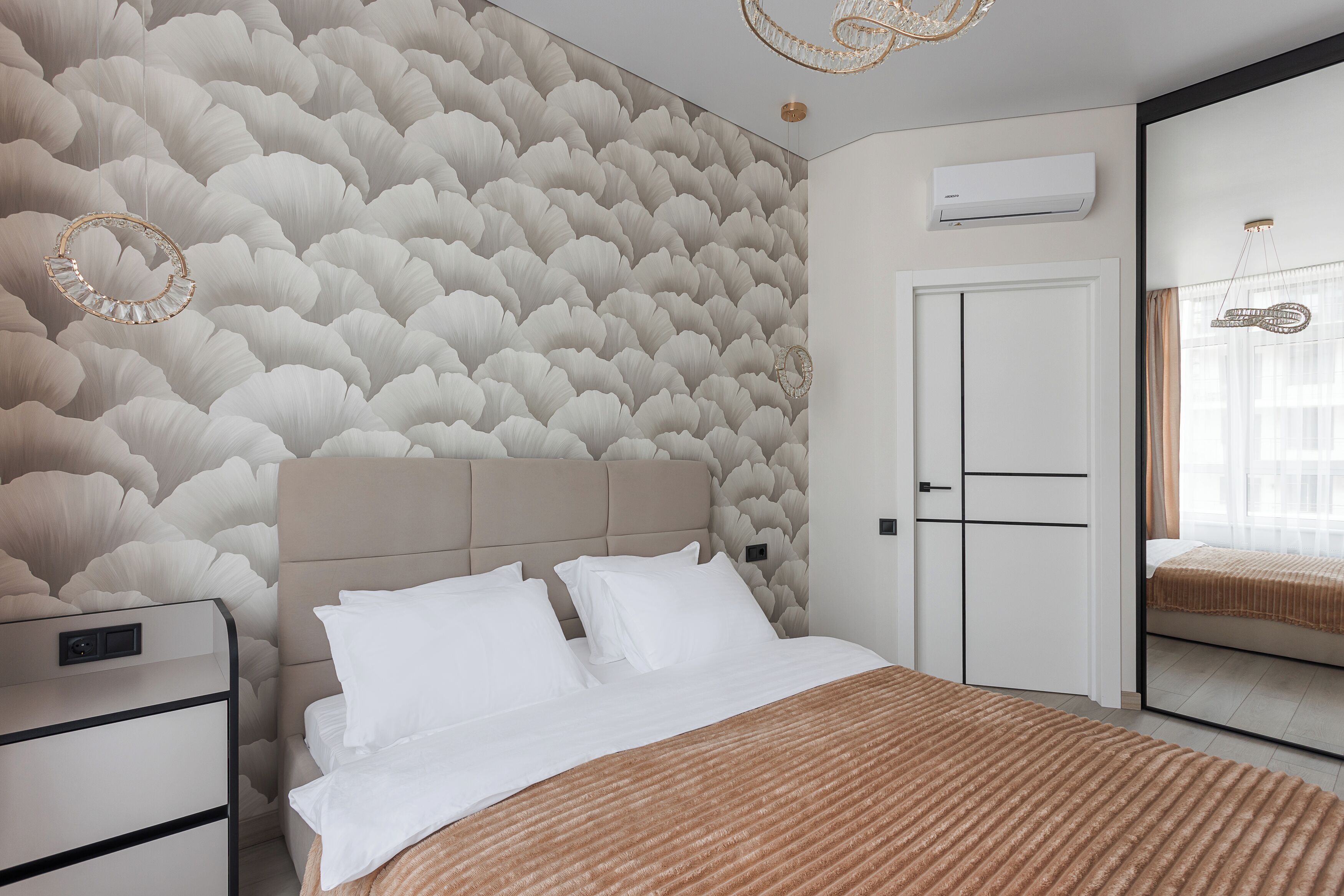 A bedroom with a patterned wallpaper, a bed with white bedding, a nightstand, a dresser, a mirror, and an air conditioning unit.