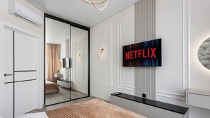 Una habitación de hotel moderna con una cama grande, un televisor montado en la pared, un espejo y una puerta corredera que da al baño.