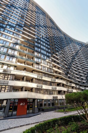 A high-rise building with multiple balconies, a prominent entrance with a red door, and a landscaped area in front. - Atmosphera ArCadia Apartments (Odesa)