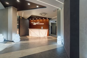 A reception area with a modern design, featuring a wooden wall with a logo, a reception desk, and a check-in counter.