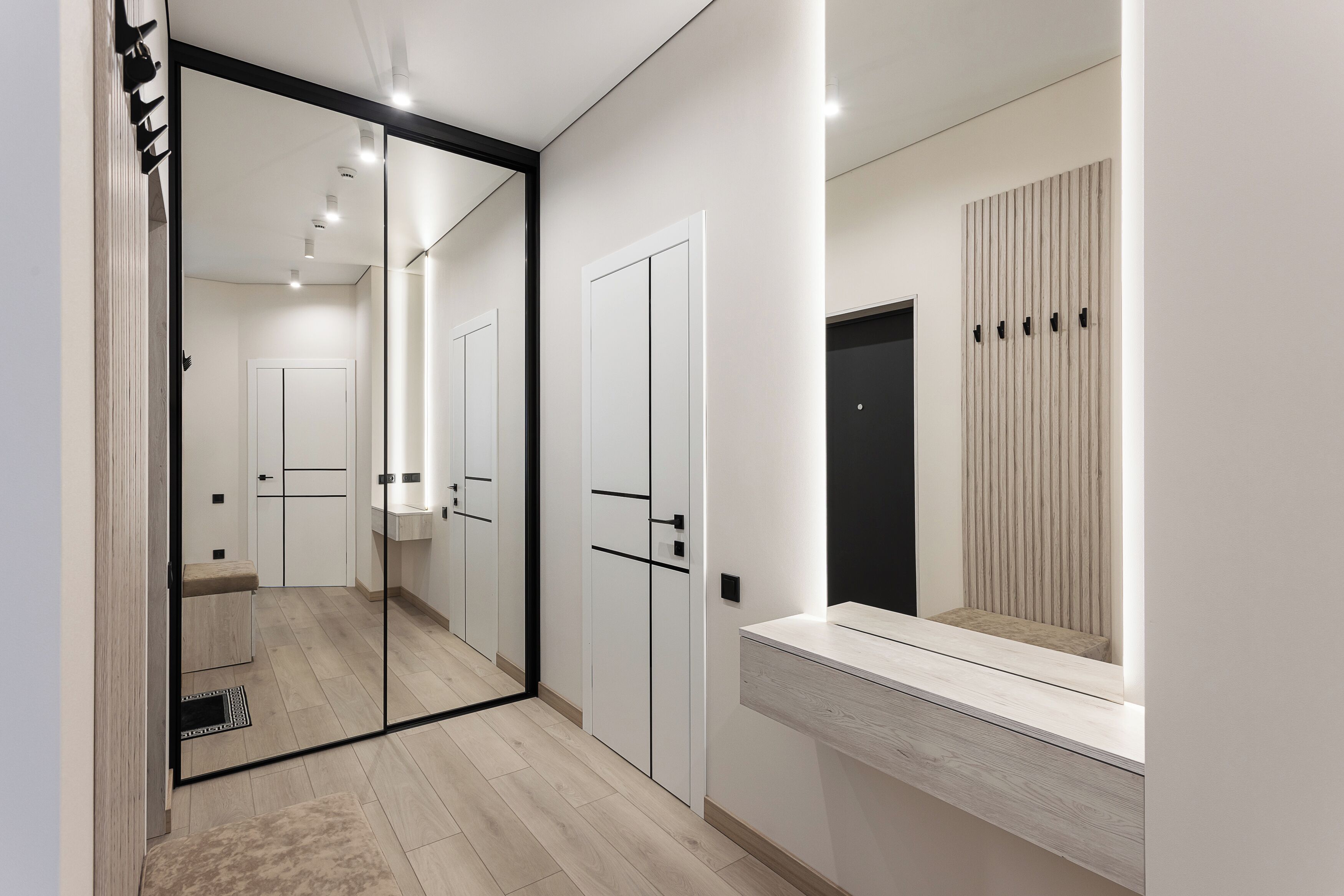 A modern hotel room with a large mirror, a wooden floor, and a built-in bench.