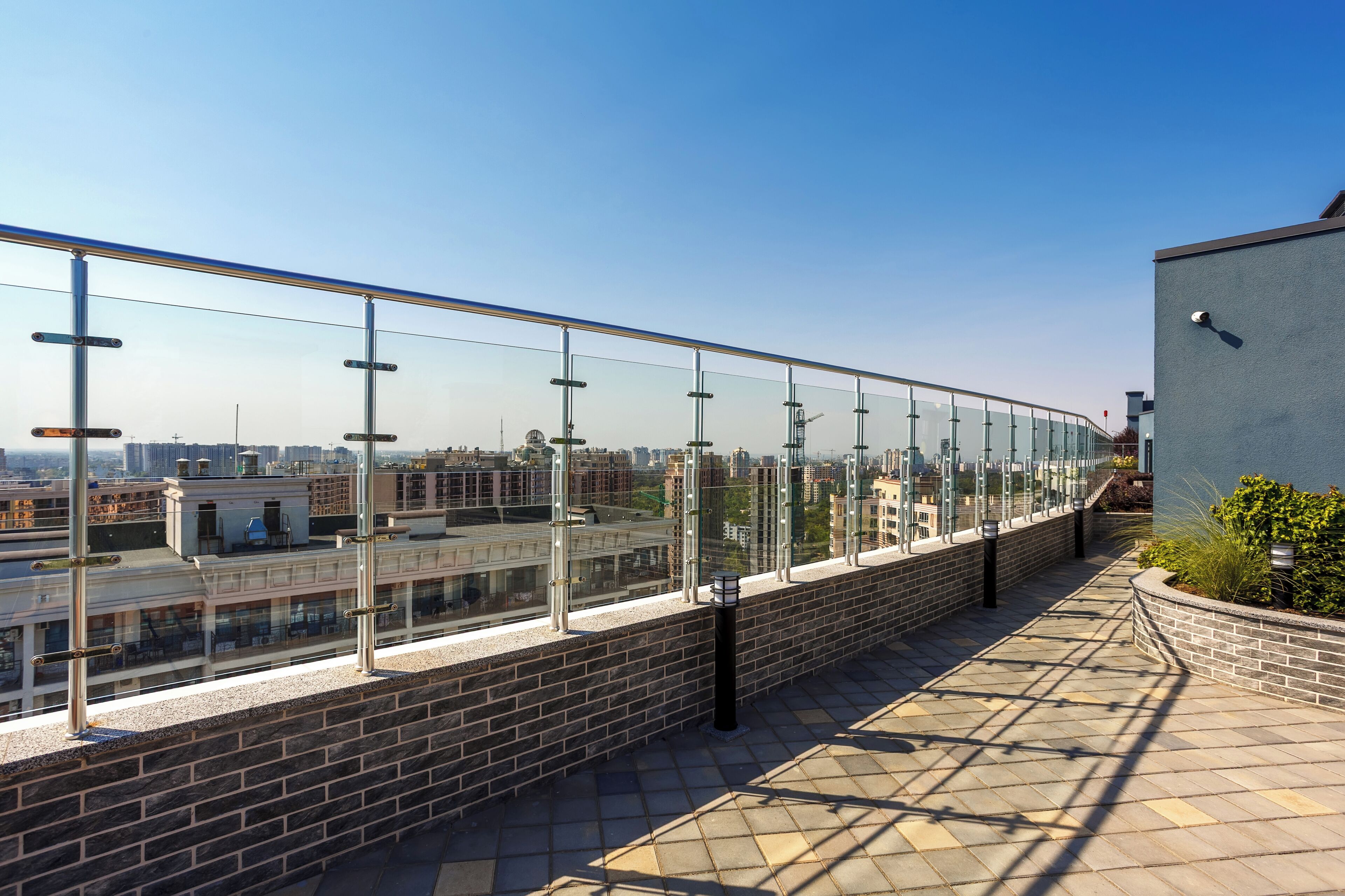 Une terrasse sur le toit dotée d’une rambarde en verre, de murs en briques et d’une allée pavée.