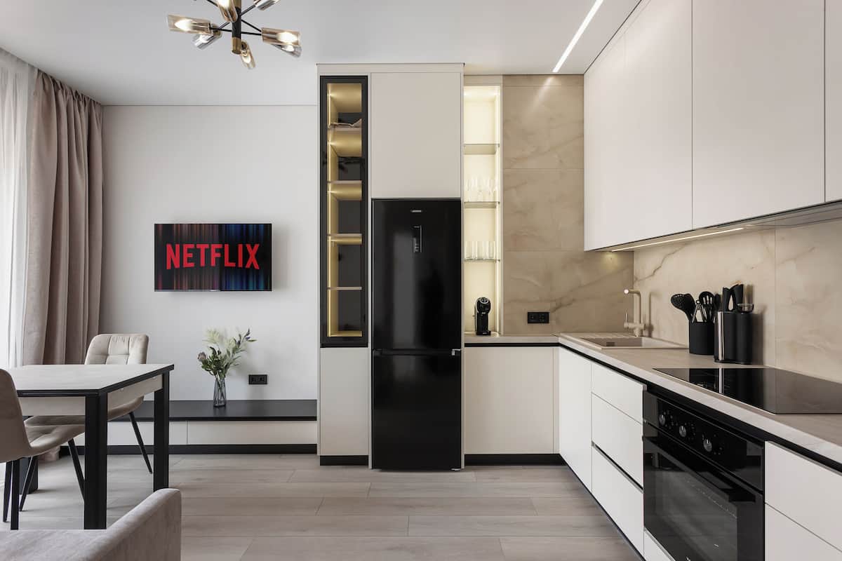 A modern kitchen with a built-in refrigerator, oven, and a dining area with a table and chairs.