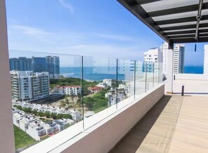 Ein Balkon mit Glasgeländer, der auf ein Wohngebiet und das Meer blickt.