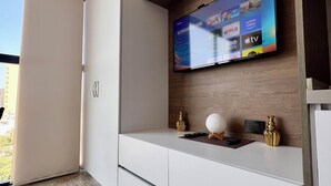 Uma sala de estar moderna com uma TV de tela plana fixada numa parede de madeira, um móvel branco embaixo e uma janela grande que oferece luz natural.
