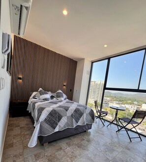 Ein modernes Schlafzimmer mit einem Bett, einer Wand aus Holzlamellen, einem großen Fenster und einem kleinen Tisch mit Stühlen.
