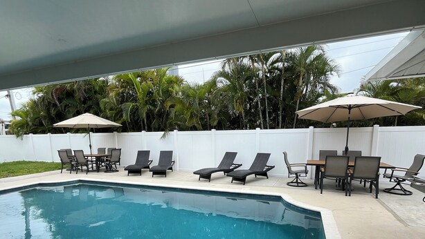 A swimming pool with lounge chairs and umbrellas, surrounded by a white fence and palm trees. - Cozy Private Unit w/ Shared Heated Pool (Cape Coral)