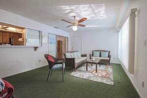 Una habitación con ventilador de techo, un sofá, una silla, una mesita y una alfombra.