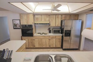 A compact kitchen with wooden cabinets, a microwave, a refrigerator, and a ceiling fan. - Cozy Private Unit w/ Shared Heated Pool (Cape Coral)