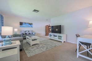 A living room with a sofa, coffee table, TV, and a dining area with a table and chairs. - Cozy Private Unit w/ Shared Heated Pool (Cape Coral)