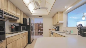 A modern kitchen with wooden cabinets, a microwave, a refrigerator, and a window with a view. - Cozy Private Unit w/ Shared Heated Pool (Cape Coral)