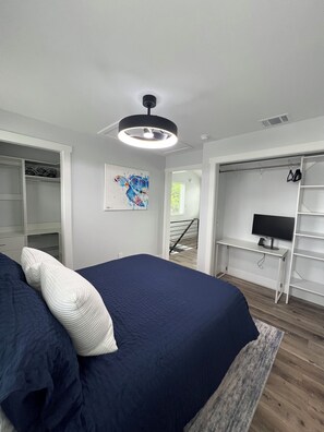 Ein Schlafzimmer mit einem Bett, einem Kleiderschrank, einem Schreibtisch mit Computer und einer Treppe, die in einen anderen Raum führt.