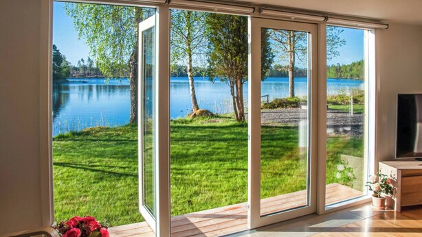 Une pièce dotée d’une grande porte-fenêtre coulissante qui donne sur un espace verdoyant, avec des arbres et une vue sur un lac.