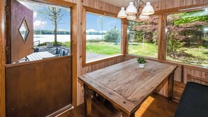 Un intérieur en bois avec une grande table, deux fenêtres donnant sur un lac et la verdure environnante, et un luminaire suspendu.