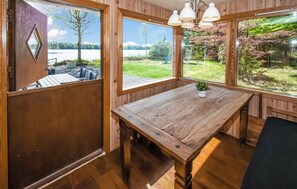 A wooden interior with a large table, two windows with views of a lake and greenery, and a hanging light fixture. - Cozy vacation home by the lake in southern Sweden (Hallaryd)