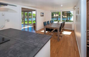 A modern kitchen with a large island, a dining area with a wooden table and chairs, and a view of a lake through large windows. - Cozy vacation home by the lake in southern Sweden (Hallaryd)