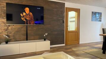 Ein modernes Wohnzimmer mit einem flachbildfernseher an einer strukturierten Wand, einer Holztür und einem kleinen Tisch mit einem Stuhl.