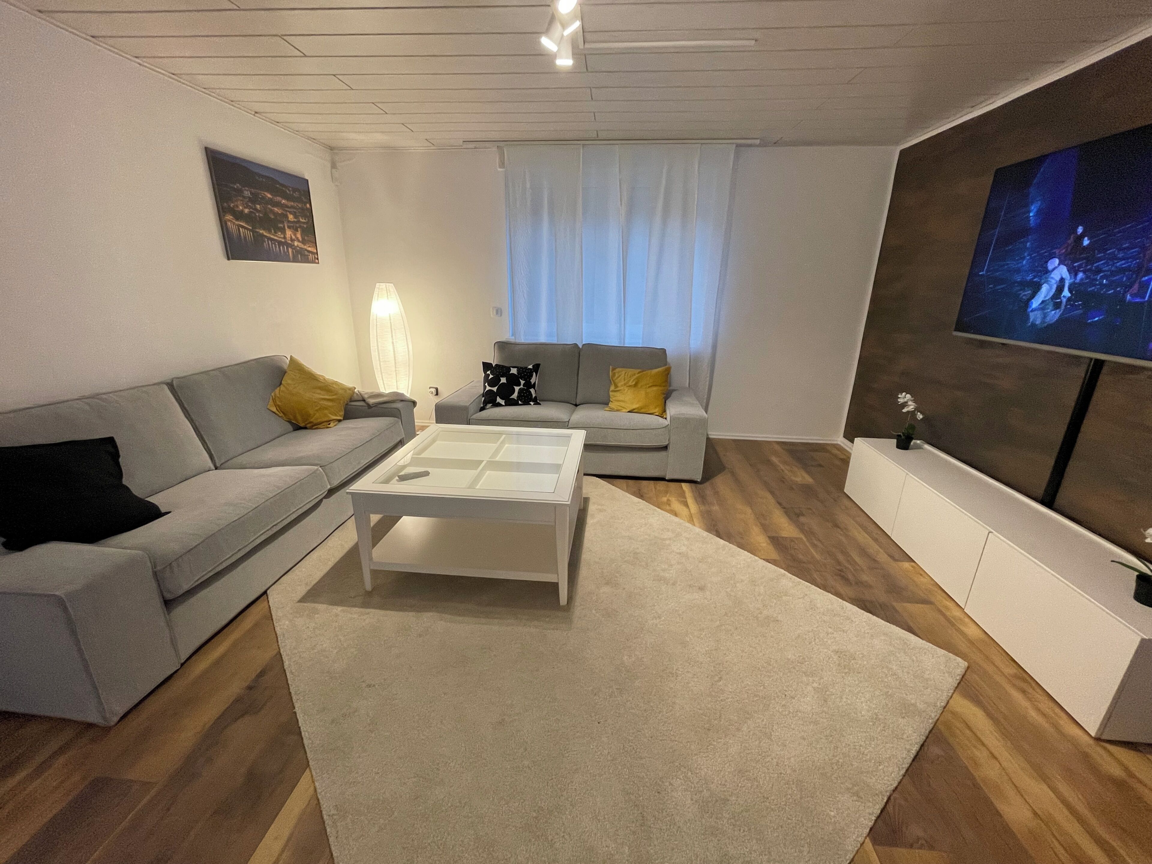 A modern living room with a grey sofa, a white coffee table, and a television mounted on the wall.