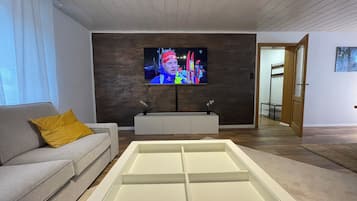 Ein modernes Wohnzimmer mit Flachbildfernseher an einer dunklen Wand, einem grauen Sofa mit gelbem Kissen und einer weißen Unterhaltungseinrichtung.