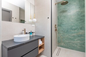 A modern bathroom with a white sink, dark countertop, and a glass-enclosed shower with green marble tiles. - Luxury villa Natali with pool, terrace and sea view (Podstrana - Sita)