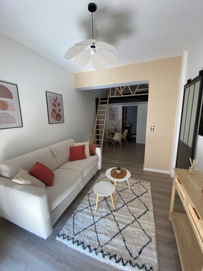 A modern living room with a white sofa, a ceiling fan, a small table with a plant, and a geometric rug. - Perched cabin (Ault)