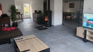 Un salon moderne avec une cheminée, un téléviseur, un coin repas et une cuisine visible au fond.
