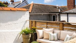 A rooftop patio with a wooden deck, a wicker sofa, and potted plants. - The Captains Penwerris - By Rowes Retreats (Falmouth)