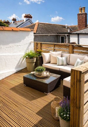 A rooftop patio with a wooden deck, a wicker sofa, and potted plants. - The Captains Penwerris - By Rowes Retreats (Falmouth)