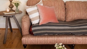 A cozy living room with a patterned sofa, a small side table with a lamp, and a coffee table with a mug and candle. - The Captains Penwerris - By Rowes Retreats (Falmouth)