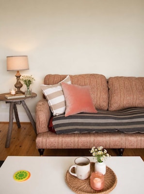 A cozy living room with a patterned sofa, a small side table with a lamp, and a coffee table with a mug and candle. - The Captains Penwerris - By Rowes Retreats (Falmouth)