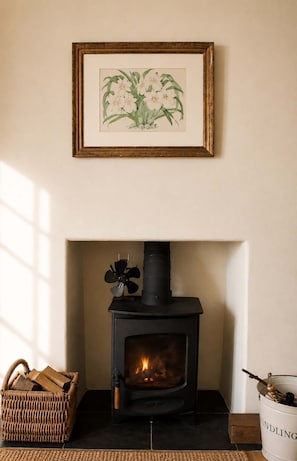 A fireplace with a black stove, a framed botanical print above it, and a wicker basket to the left. - The Captains Penwerris - By Rowes Retreats (Falmouth)