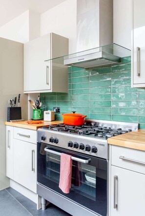 A kitchen with a gas stove, oven, and a green tiled backsplash. - The Captains Penwerris - By Rowes Retreats (Falmouth)