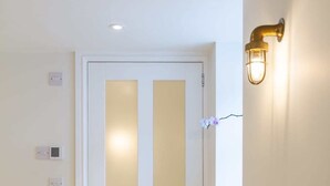 A white door with a frosted glass panel, a wall-mounted light fixture, and a power outlet. - The Captains Penwerris - By Rowes Retreats (Falmouth)