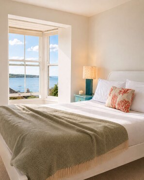Une chambre à coucher avec un lit, une table de chevet, une lampe et une vue sur la mer.