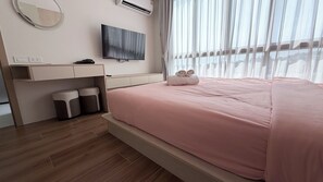 Ein modernes Hotelzimmer mit Bett, Fernseher, Schreibtisch mit Stuhl und einem Fenster mit Vorhängen.
