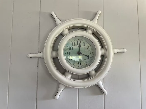 Reloj de pared con temática náutica, que presenta un diseño de timón y esfera redonda con números romanos.