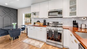 Una cucina moderna con mobili bianchi, elettrodomestici in acciaio inossidabile e un'area pranzo con tavolo e sedie neri.