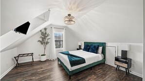 Una camera da letto con un soffitto spiovente, un letto con testiera verde, un comodino, una lampada e una pianta in vaso.