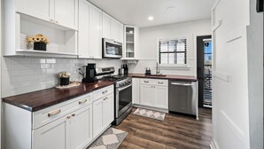Cucina con mobili bianchi, microonde, piano cottura e lavastoviglie.