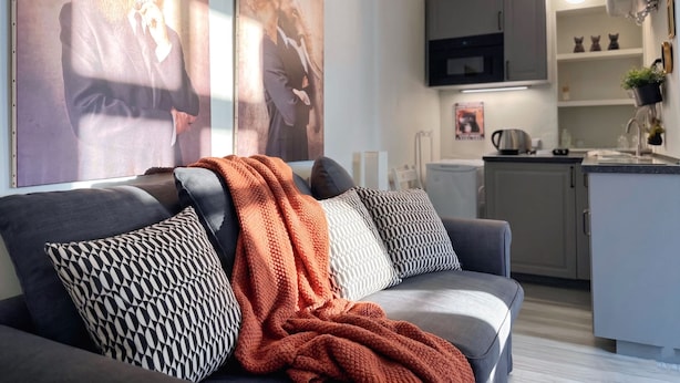 Uma sala de estar moderna com um sofá cinzento, almofadas estampadas e um cobertor de tricô.