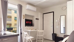 Um apartamento moderno com cozinha compacta, sala de jantar com mesa e cadeiras, sala de estar com sofá, televisão na parede e porta com telefone e espelho.