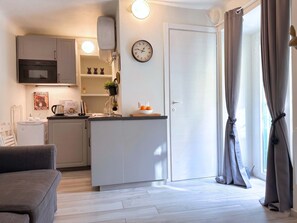 A compact kitchen with a built-in oven, a clock, and a small island with fruit. - Casa Caterina - in the Heart of Porta Venezia (Milan)