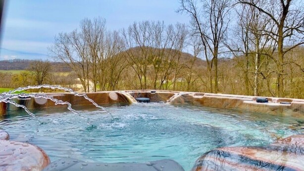 A hot tub with a view of trees and hills in the background. - Wexford Hollow 6 BR Cabin with Swimming Pool & Hot Tub (Lansing)